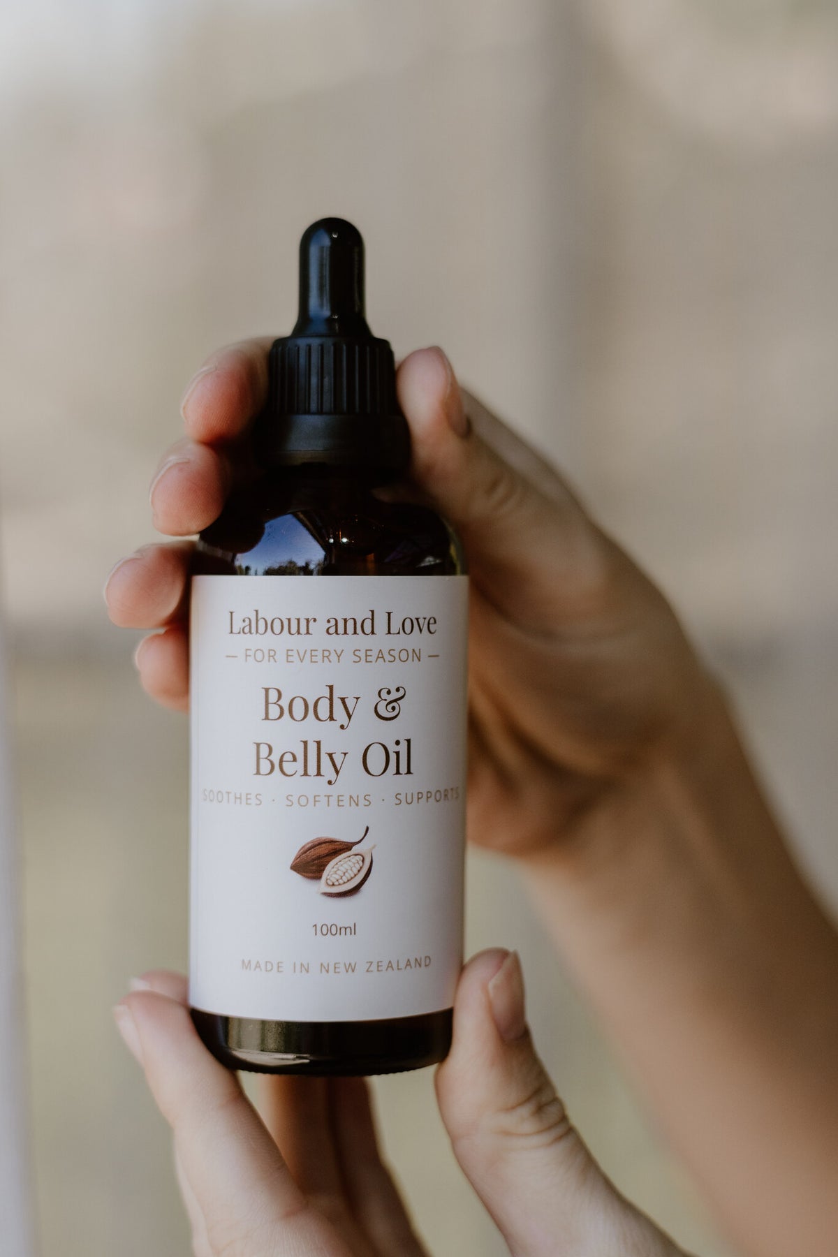 Close-up of hands holding Labour & Love Body & Belly Oil dropper bottle, a natural pregnancy skin oil from NZ