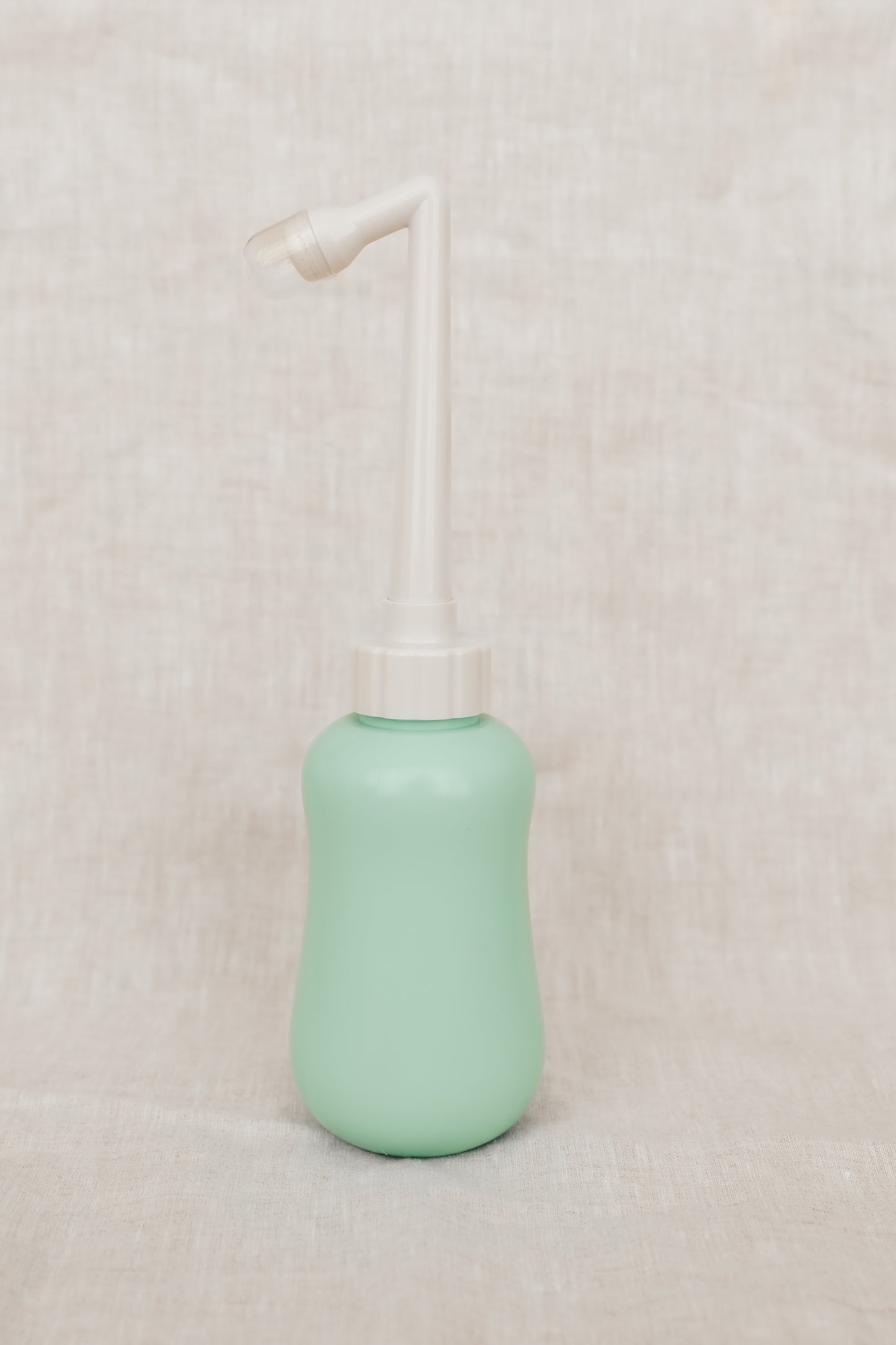 Mint green peri bottle with a white pump on a beige background