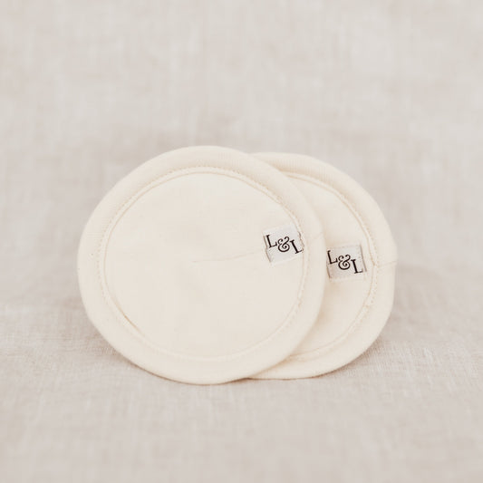 Two round organic cotton breast pads with branding on a beige background