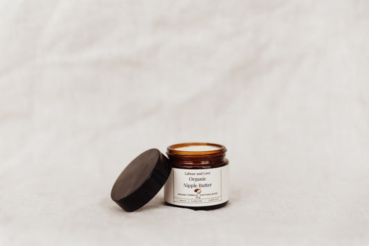 Open jar of organic nipple butter with a black lid on a light gray background.
