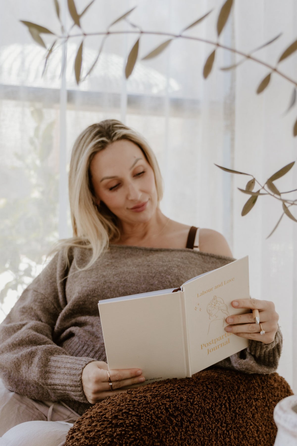 New mum sitting by a window reading her Labour and Love postpartum journal