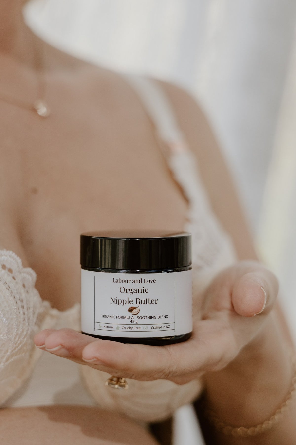 Woman in a nursing bra holding a jar of Labour & Love Organic Nipple Butter, a lanolin-free breastfeeding balm