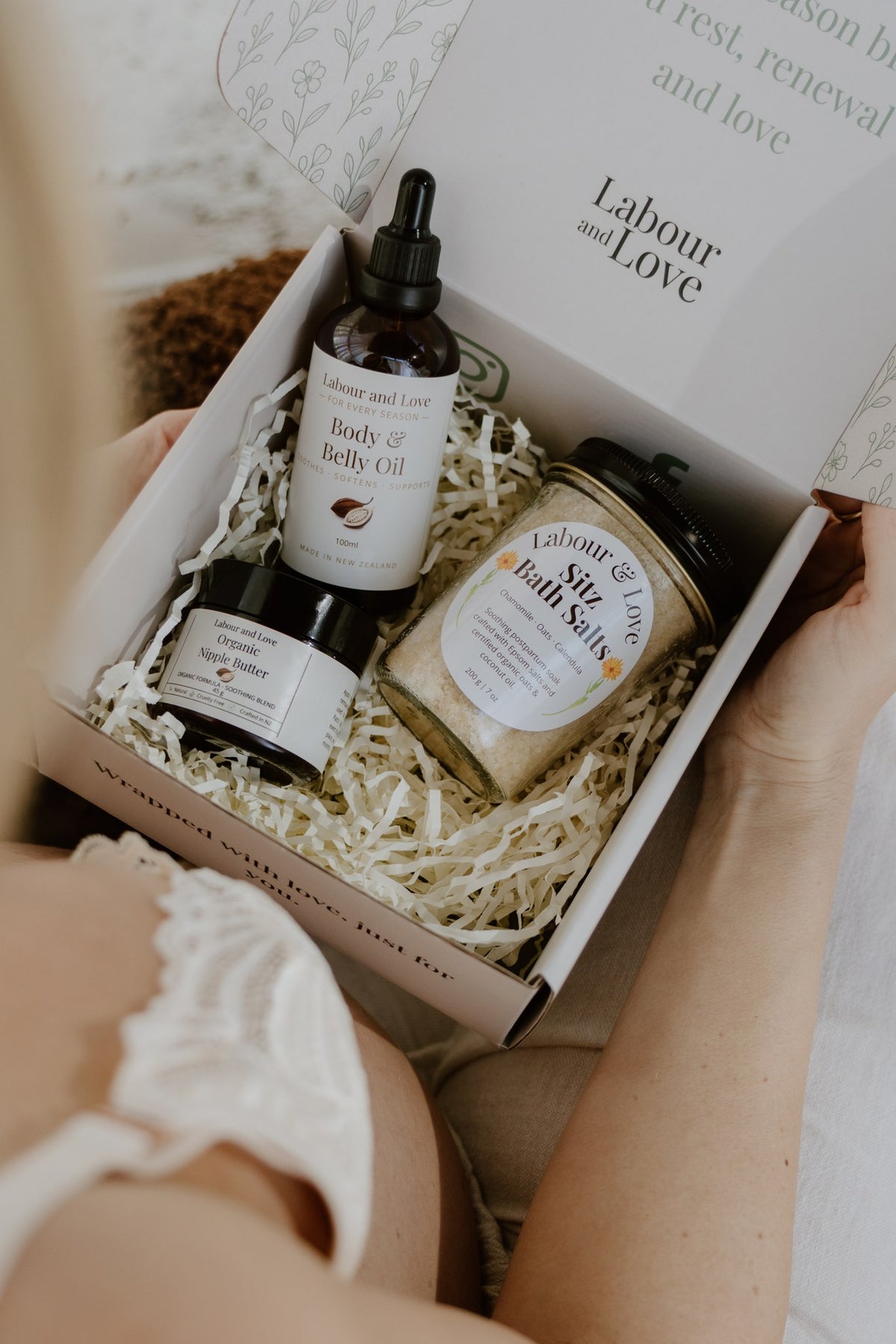 Over-the-shoulder view of a new mum opening the Gentle Beginnings gift box with belly oil, sitz bath salts and nipple butter