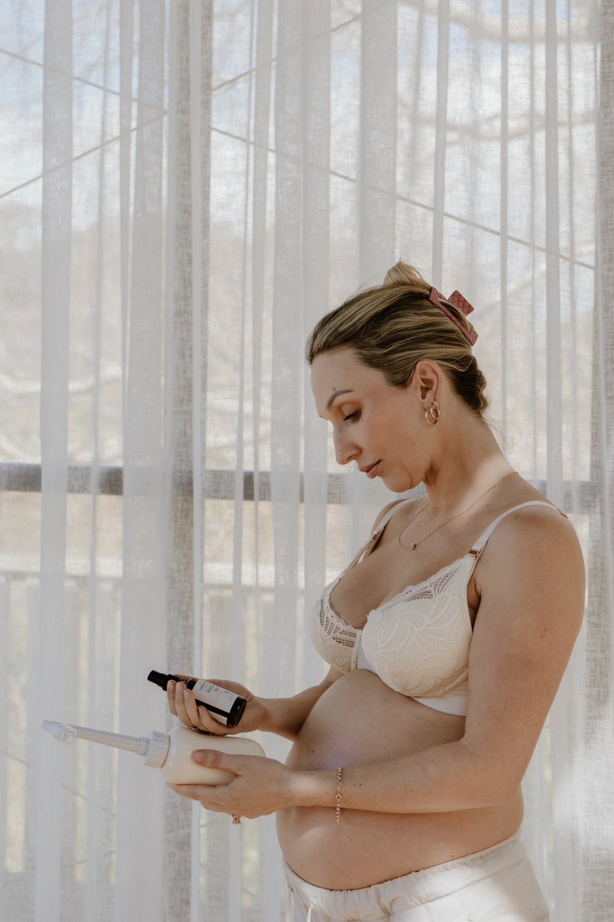 Pregnant woman reading the label of Labour & Love Perineum Relief Spray while preparing her postpartum recovery kit