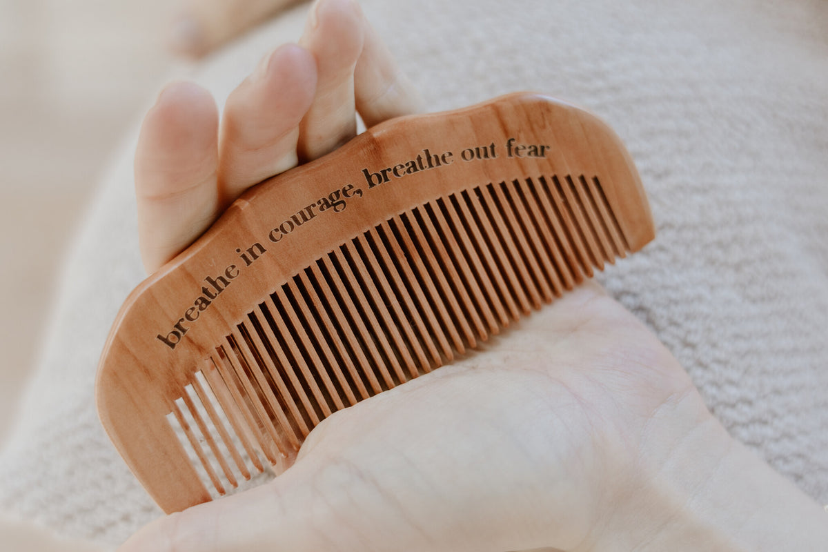Wooden birth comb engraved with an affirmation, held in an open palm, natural labour pain relief tool