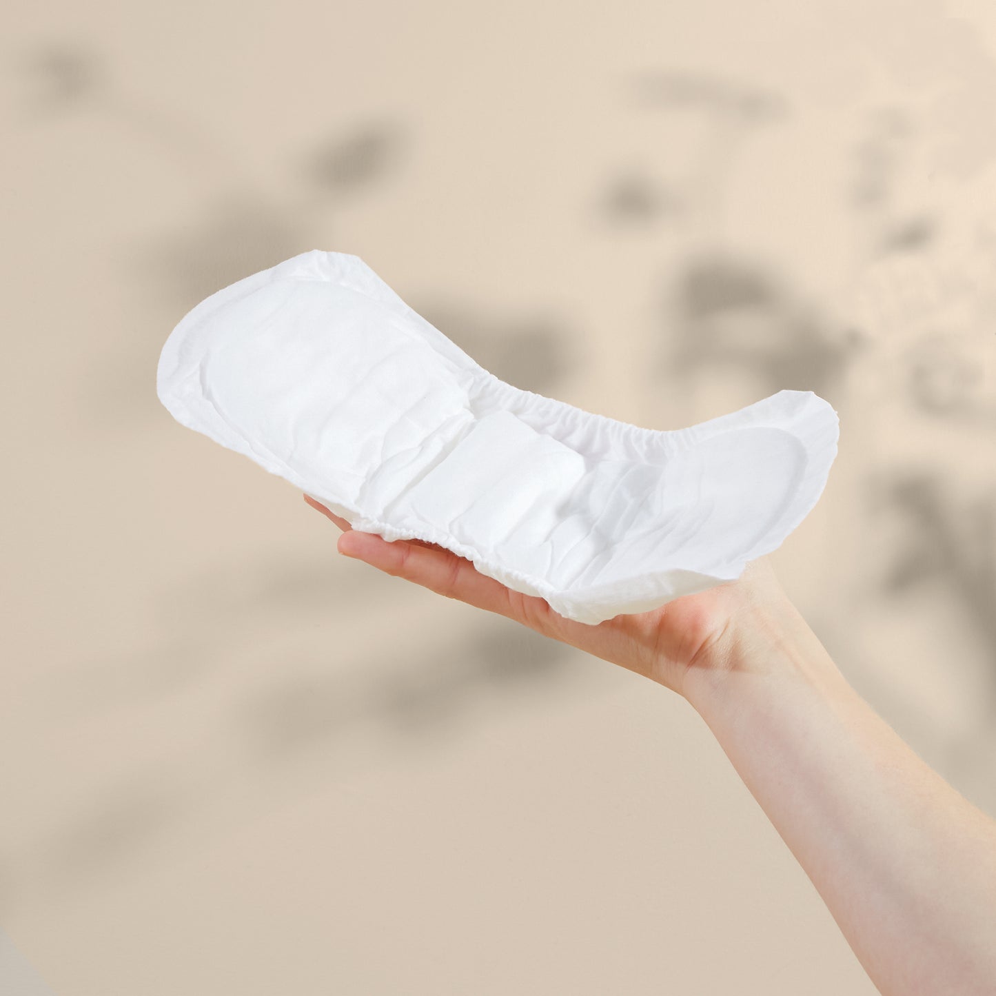White Maternity pad held in a hand against a beige background