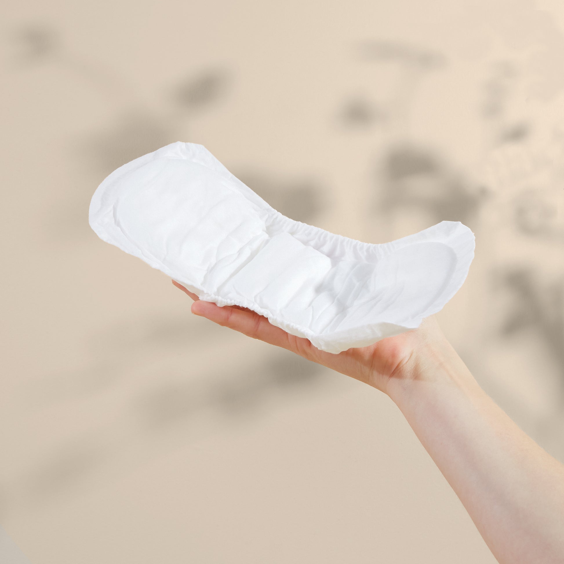 White Maternity pad held in a hand against a beige background