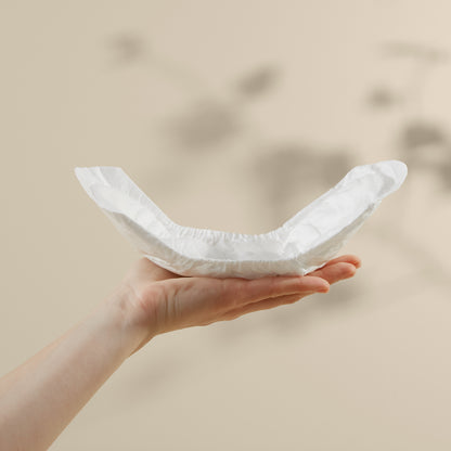 Hand holding a folded white maternity pads against a beige background