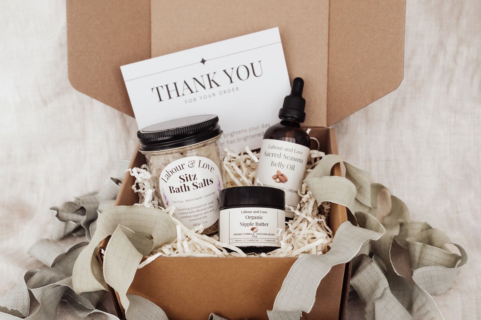 Gift box with bath salts, organic belly oil, organic nipple butter and a 'Thank You' card on a soft background