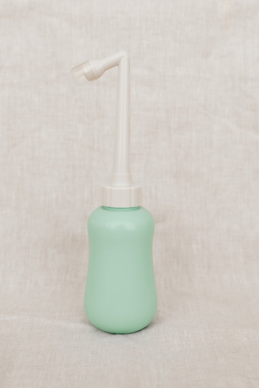 Mint green peri bottle with a white pump on a beige background
