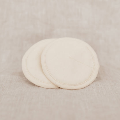 Two beige organic cotton breast pads on a linen background