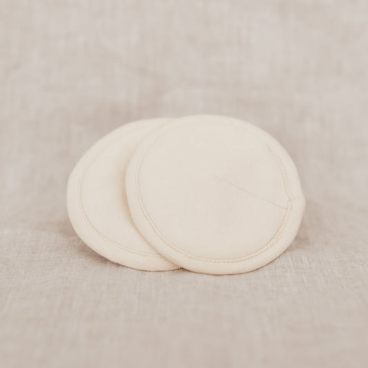 Two beige organic cotton breast pads on a linen background