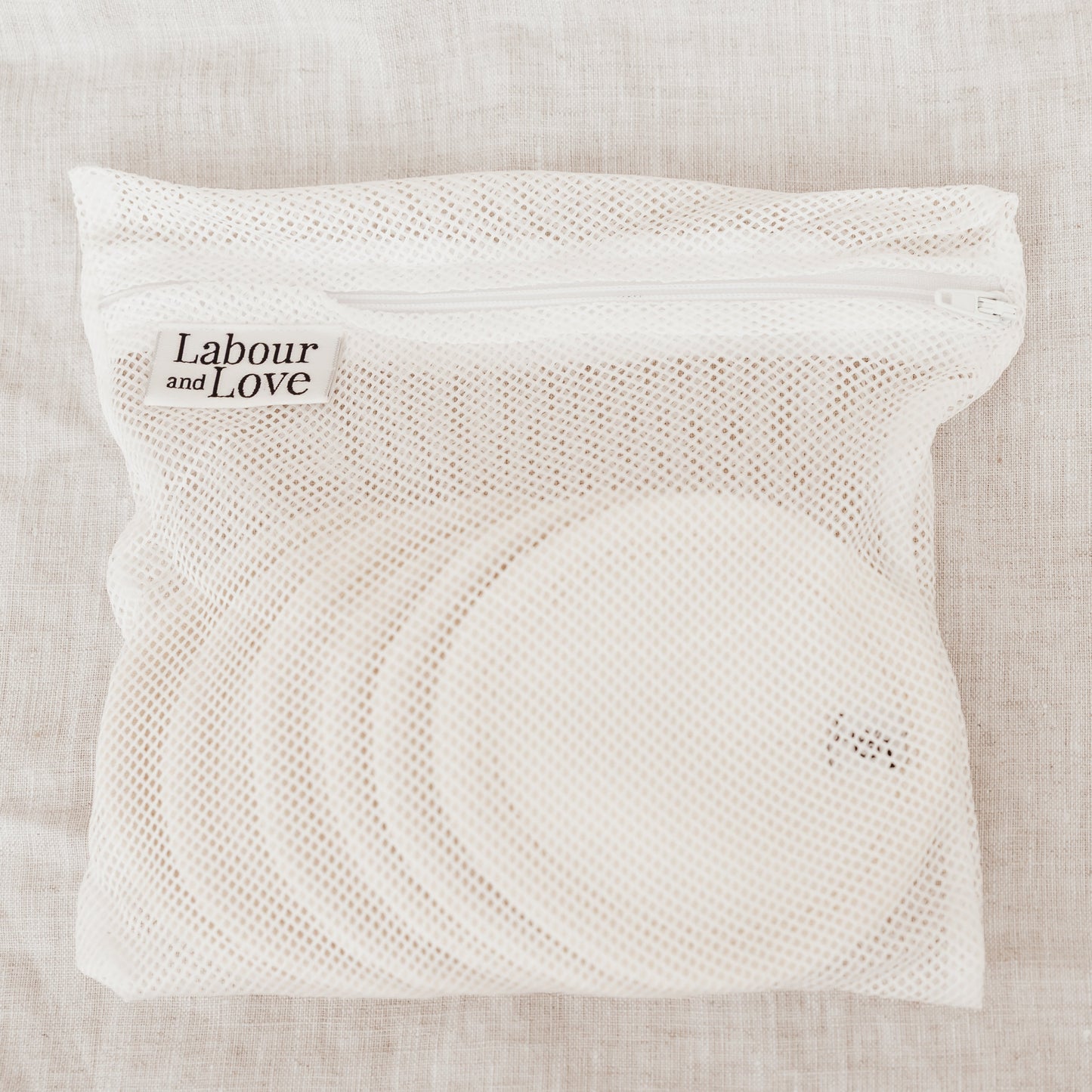 White mesh bag with 'Labour and Love' branding on a beige fabric background