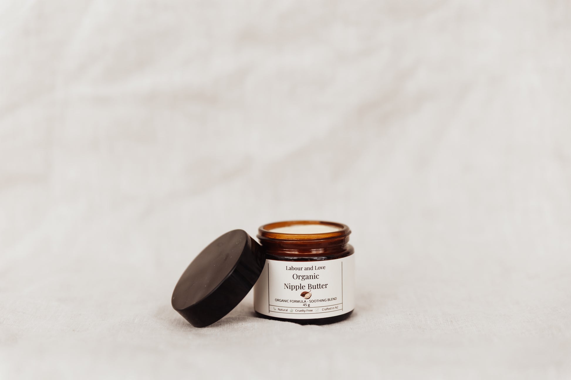 Open jar of organic nipple butter with a black lid on a light gray background. 