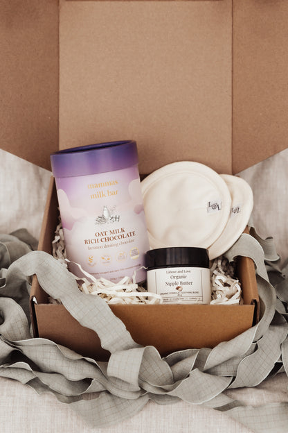 Box of skincare products including organic nipple butter, breast pads, and a Oat choc lactation powder on a soft fabric background.