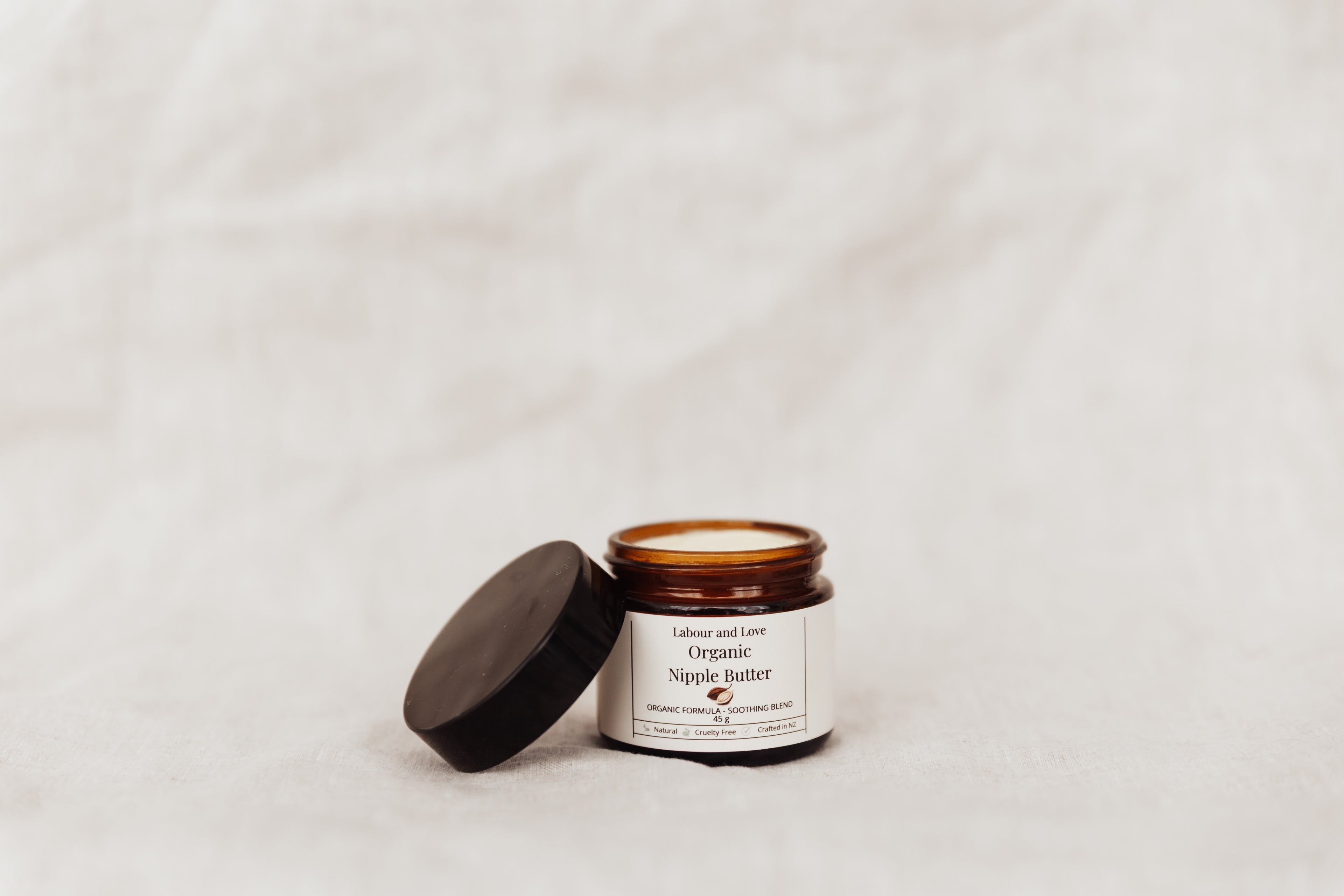 Open jar of Labour and Love organic nipple butter on soft natural fabric — lanolin-free breastfeeding balm