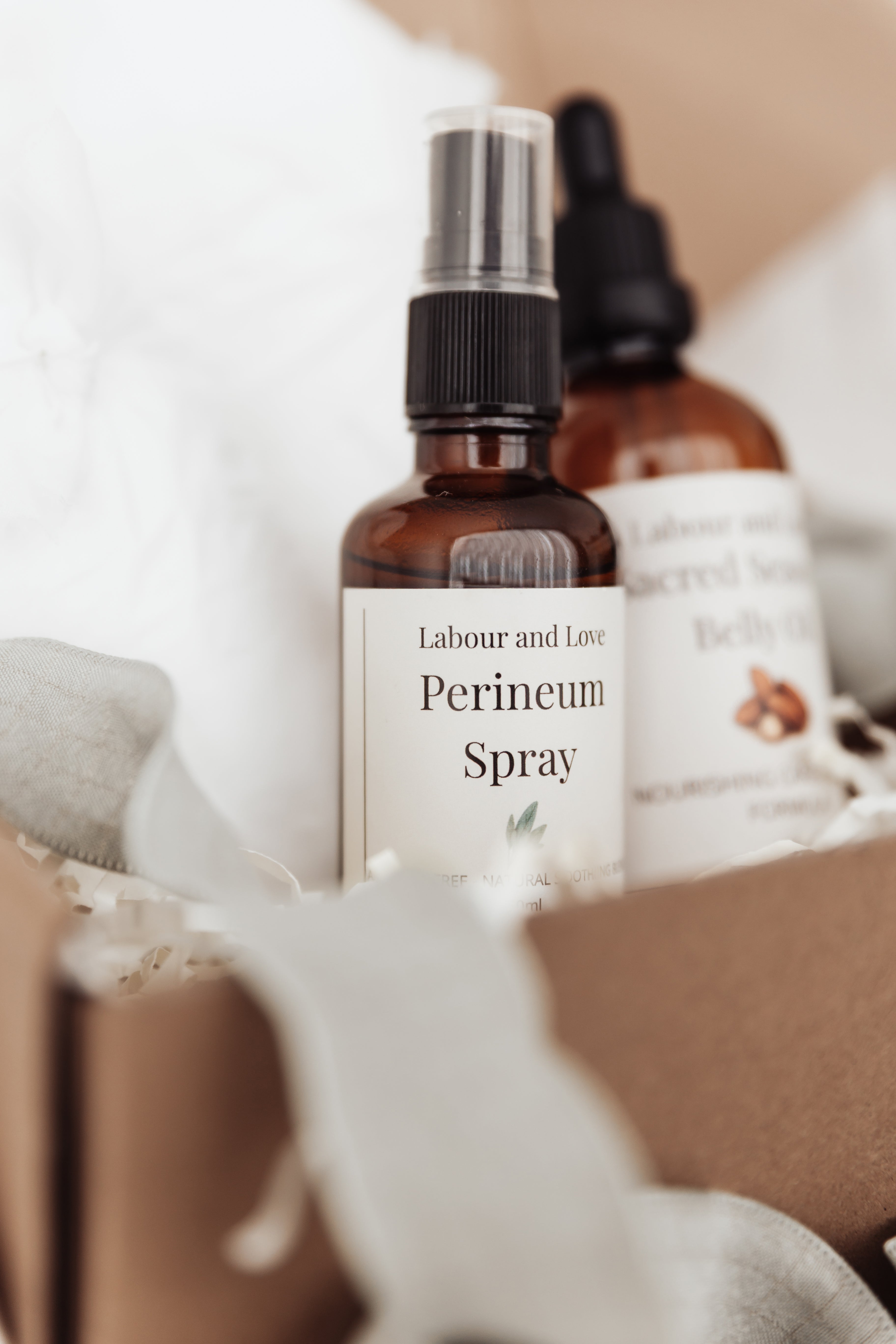 Labour and Love perineum relief spray in focus, with a bottle of organic belly oil softly blurred behind — natural pregnancy and postpartum care