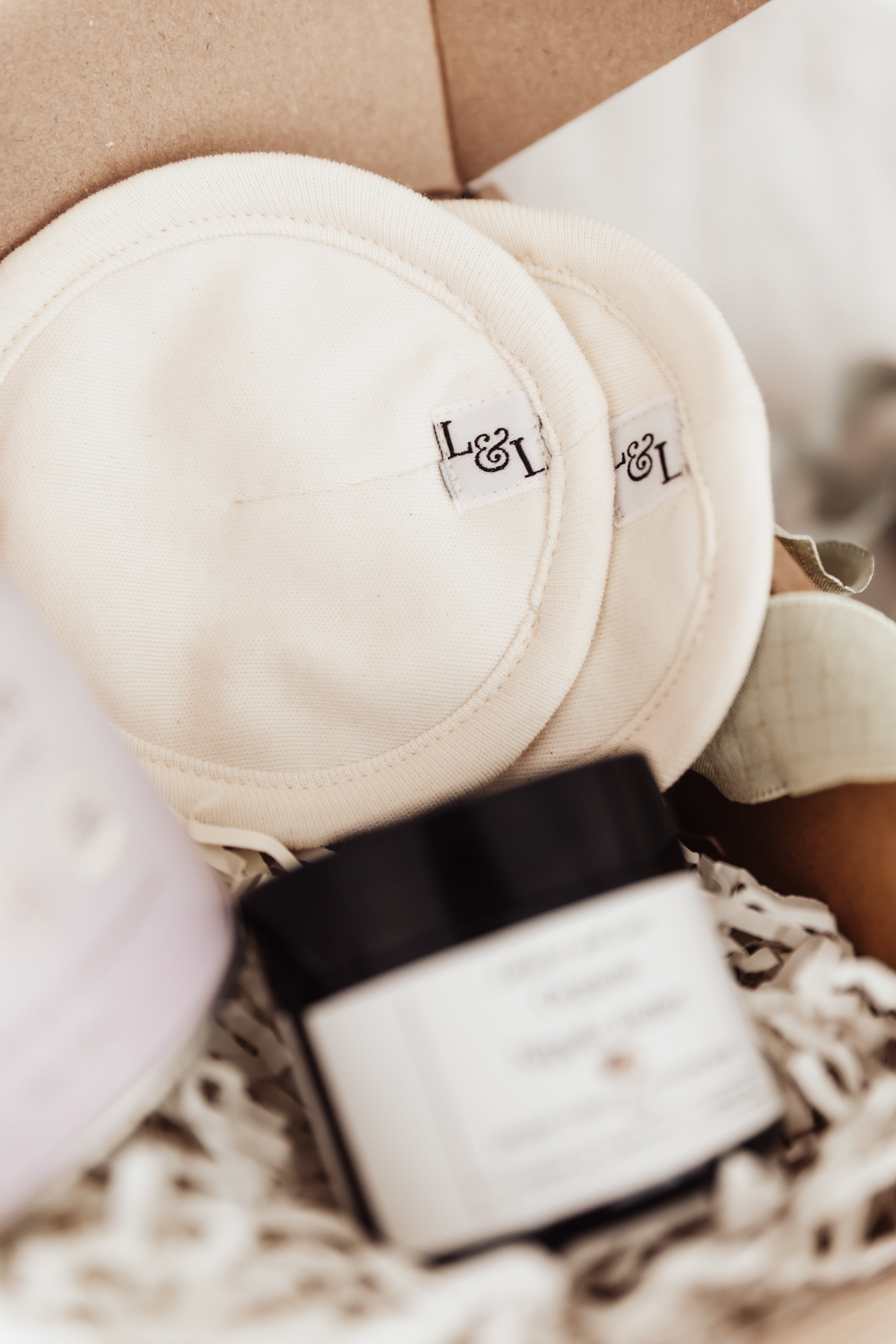 Labour and Love organic cotton and wool reusable breast pads in focus, with a jar of nipple butter softly blurred behind — natural breastfeeding care